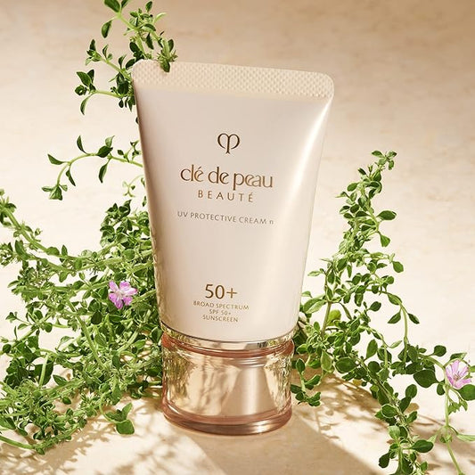 Clé de Peau UV Protective Cream with green leaves and flowers on a beige background